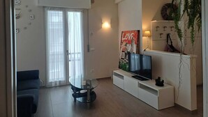 A modern living room with a glass table, a flat-screen TV, a sofa, and a door with a view. - Dimora Paola - Garda - Centro con parcheggio- ac (Garda)