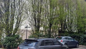 A parking area with two parked cars, surrounded by trees and a building with a sloped roof. - Dimora Paola - Garda - Centro con parcheggio- ac (Garda)