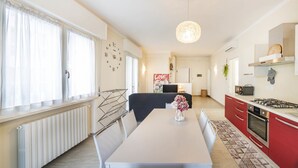 A modern kitchen with a dining area, featuring a white table, red cabinets, and a hanging light fixture. - Dimora Paola - Garda - Centro con parcheggio- ac (Garda)