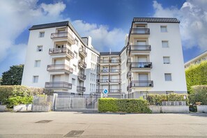 Un immeuble résidentiel à plusieurs étages, doté de balcons, d’une entrée sécurisée et surplombant un ciel dégagé.