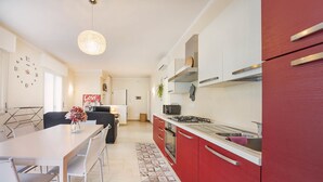 A modern kitchen with red cabinets, a white countertop, and a dining area with a table and chairs. - Dimora Paola - Garda - Centro con parcheggio- ac (Garda)