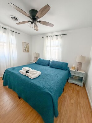 Une chambre à coucher comprenant un lit, un ventilateur de plafond, une table de chevet et une commode.