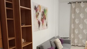 A living room with a grey sofa, a wooden bookshelf, a small round table, and a floral curtain. - A&N Valle Niza (Benajarafe)