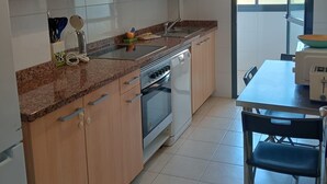 A kitchen with wooden cabinets, a countertop, a sink, an oven, and a dining table with chairs. - A&N Valle Niza (Benajarafe)