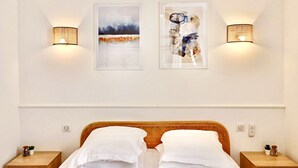 A hotel room with a bed, two wall-mounted light fixtures, and two framed artworks.