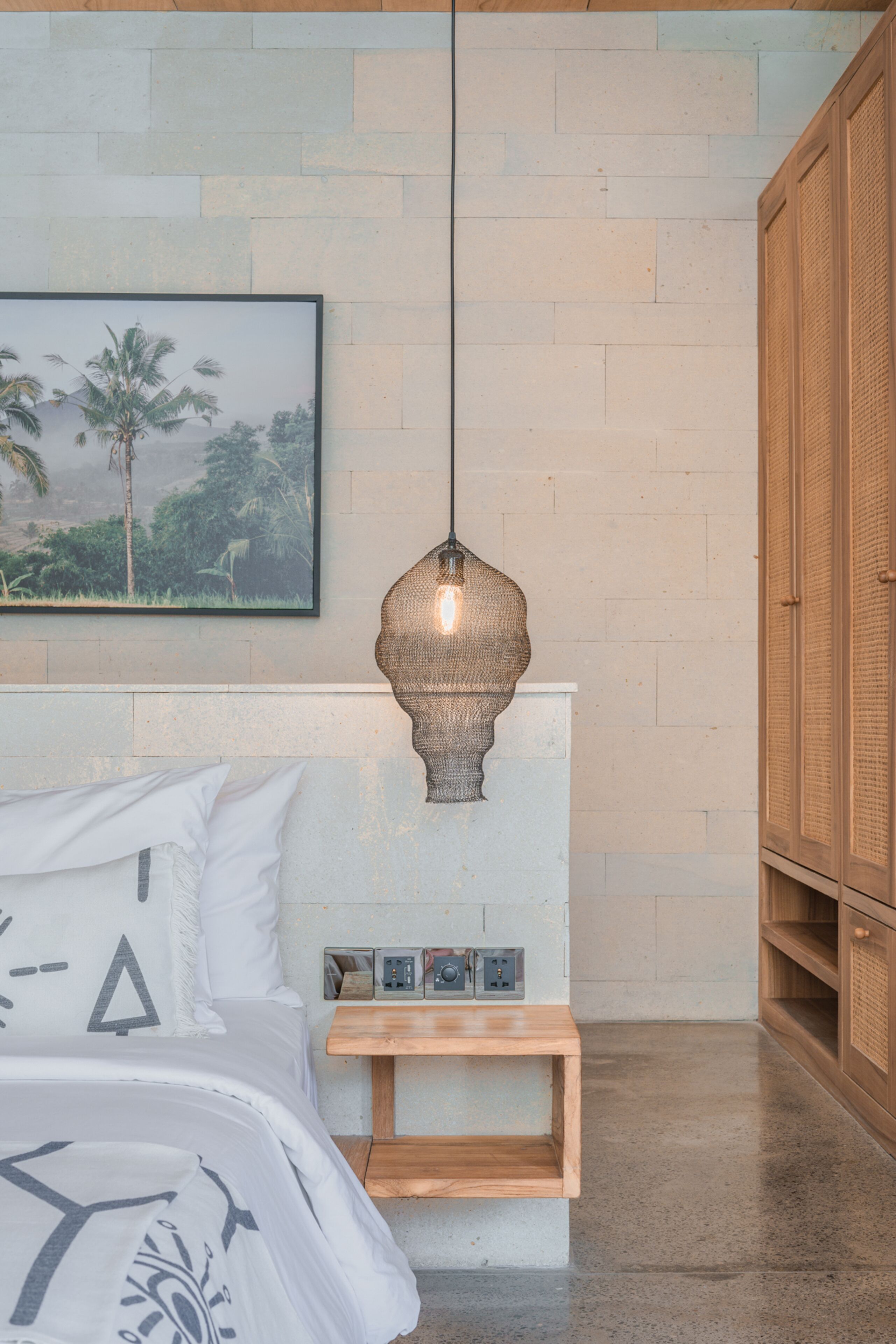 Une chambre à coucher comprenant un lit, une table de chevet, un luminaire fixé au mur et une armoire en bois.