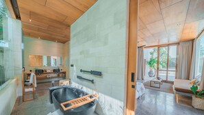 A modern bathroom with a large black bathtub, wooden shelves, and a mirror. - Villa Boya (Canggu)