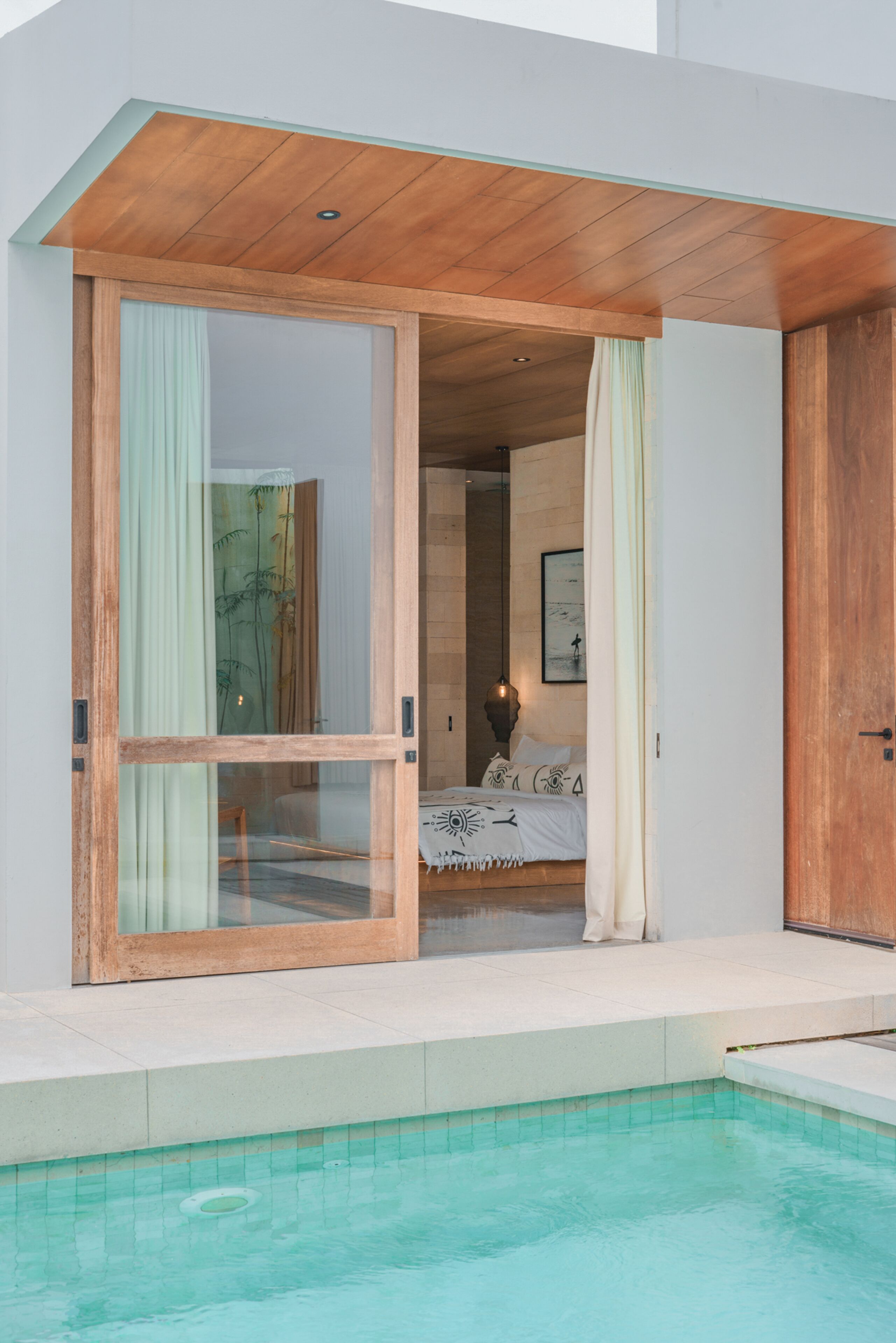 A modern hotel room with a large sliding glass door leading to a private balcony with a pool.