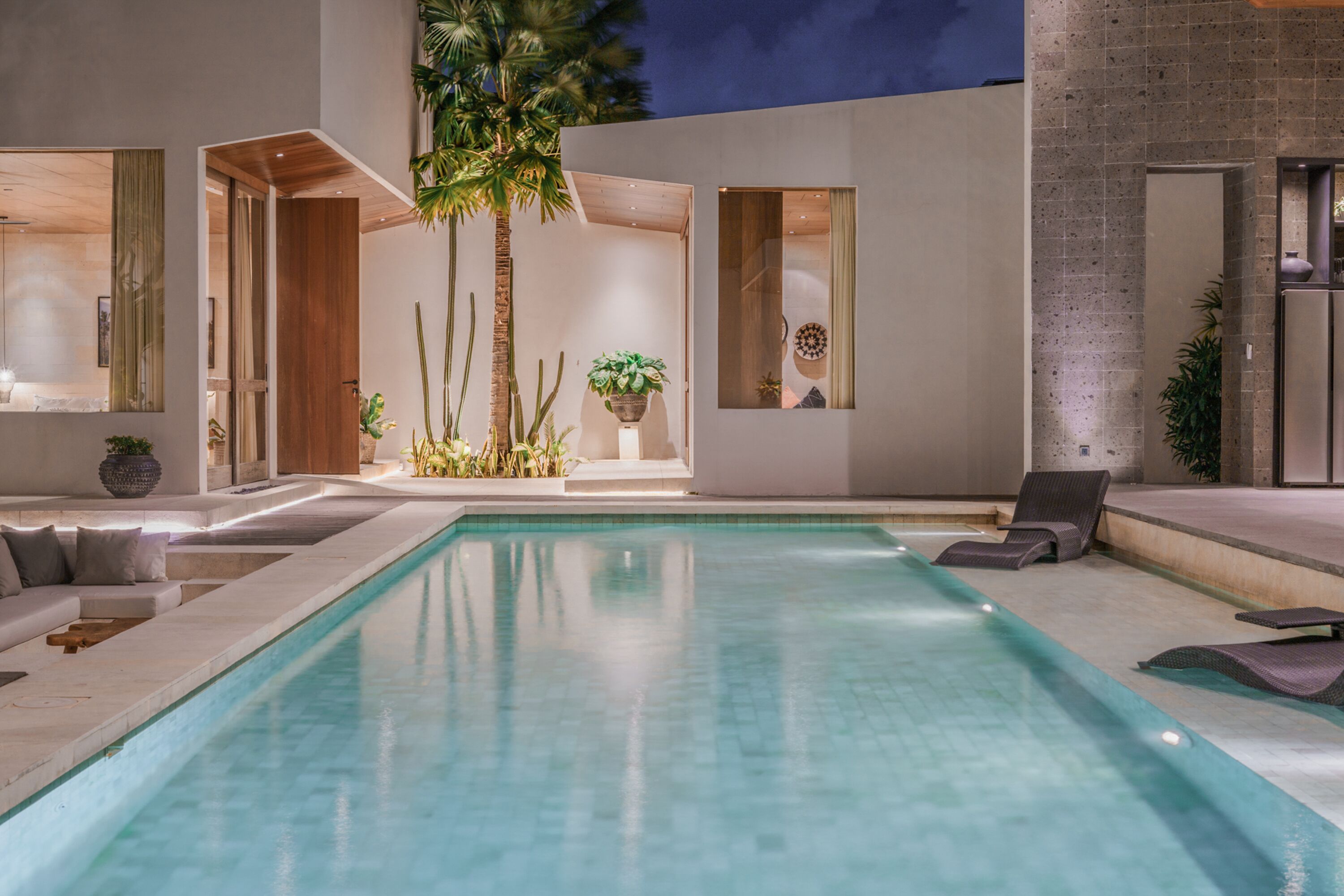 Uma área interna de piscina moderna, com piscina transparente, espreguiçadeiras e plantas em vasos.