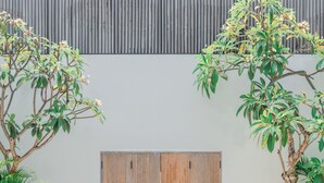 A pool area with a wooden door, two palm trees, and a white tiled deck. - Villa Boya (Canggu)