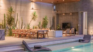 A modern outdoor pool area with lounge chairs, a dining table, and various plants. - Villa Boya (Canggu)