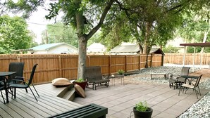 Une terrasse en bois, agréée de mobilier d’extérieur, notamment d’un banc et de chaises, entourée d’une clôture en bois et d’arbres.