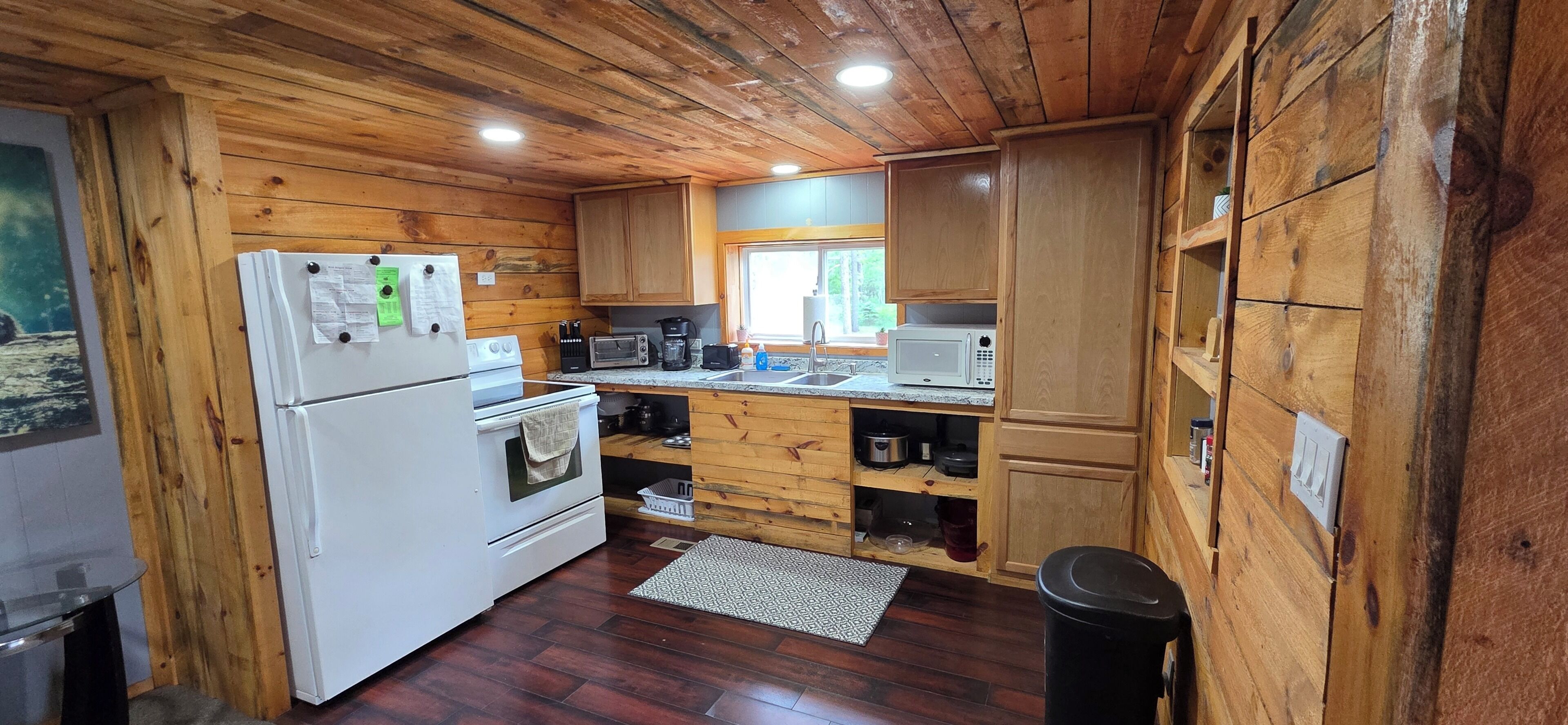 Una cocina tipo cabaña con paredes de madera, refrigerador, estufa, microondas y pileta.