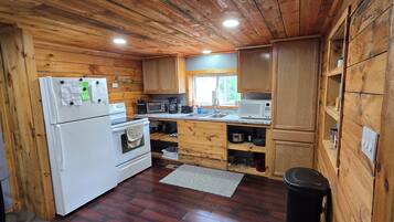 Una cocina tipo cabaña con paredes de madera, refrigerador, estufa, microondas y pileta.