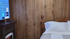 Une pièce aux murs lambrissés, avec un lit, un téléviseur posé sur un meuble et une cheminée.