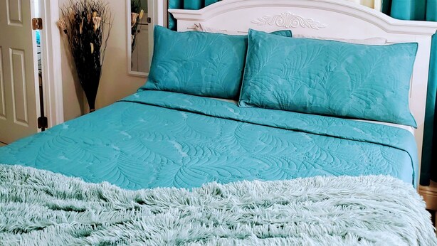 Une chambre à coucher avec un lit, une literie de couleur turquoise, une tête de lit blanche et des rideaux turquoise.
