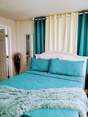 A bedroom with a bed, teal bedding, a white headboard, and teal curtains. - Rest apartament (Holiday)