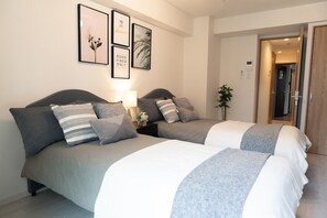 A hotel room with two beds, a bedside table with a lamp, and framed artwork on the wall.