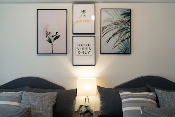 A bedroom with a bed, pillows, a bedside table with a lamp, and three framed pictures on the wall.