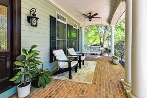 A covered porch with brick flooring, two white chairs, a bench, and potted plants. - Lake Norman Cove Home w/ Golf Sim & Kayaks (Sherrills Ford)