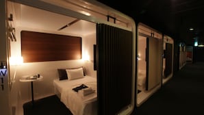 Una habitación de hotel moderna con cama, mesita de noche y un amplio ventanal con cortinas.