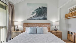 Un dormitorio con una cama grande, dos mesitas de noche con lámparas, un cabecero de madera y una obra de arte colgada en la pared que representa una ola.