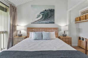 A bedroom with a large bed, two bedside tables with lamps, a wooden headboard, a wall-mounted artwork of a wave, and a wooden crib. - Turtle Bay Townhouse Steps to the Beach! (Kahuku)