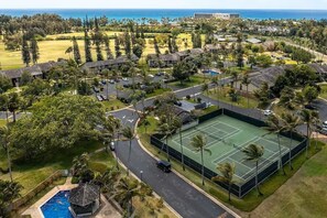 An aerial view of a resort with a tennis court, pool, and beachfront.