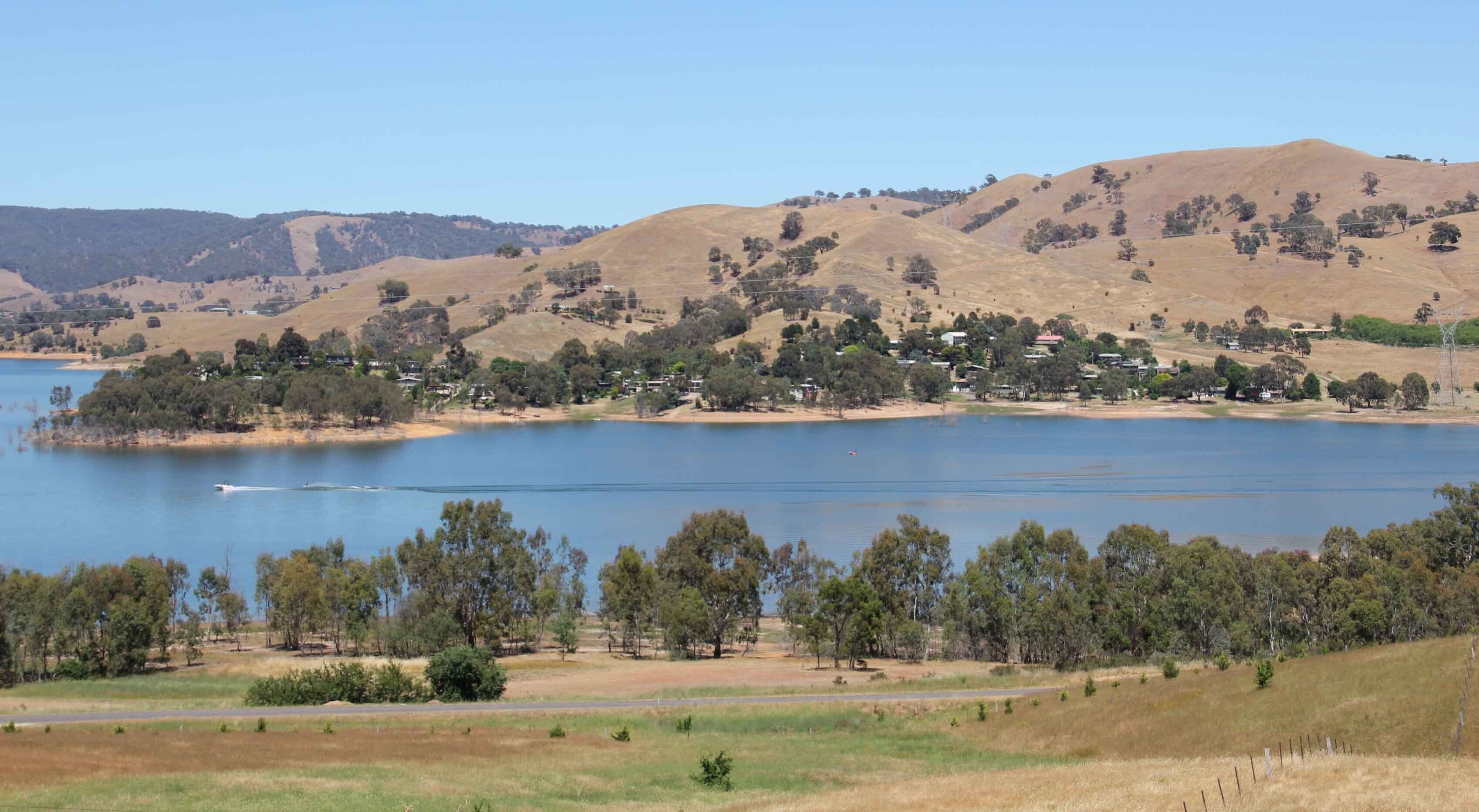 Un lago con un pequeño pueblo en la orilla, rodeado de colinas.