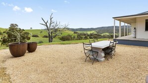 A gravel patio with a table and chairs, two large planters, and a house with a porch overlooking a green landscape. - Manandel - Rural Retreat (Bonnie Doon)