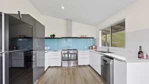A modern kitchen with a stainless steel refrigerator, oven, and dishwasher, white cabinetry, and a window overlooking a green landscape. - Manandel - Rural Retreat (Bonnie Doon)