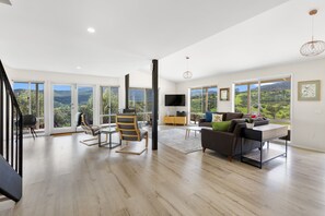 Un salon spacieux avec un grand canapé, une table basse et un téléviseur. De nombreuses fenêtres offrent une vue sur l’extérieur.