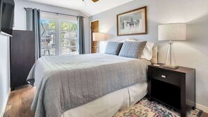Een slaapkamer met een bed, een nachtkastje, een lamp, een plafondventilator, een raam met gordijnen, en een lijst met een foto aan de muur.