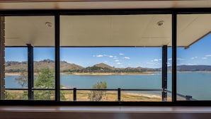 Blick aus einem Zimmer mit großen Fenstern auf einen See, Hügel und einen Strand.