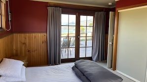 Un dormitorio con cama, cabecera de madera, vista al exterior a través de un ventanal y teléfono en la pared.