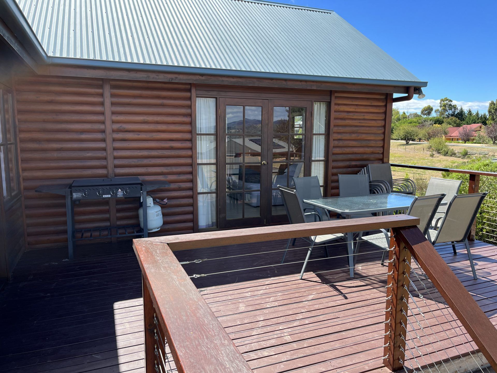 A wooden cabin with a deck, a table with chairs, and a grill.