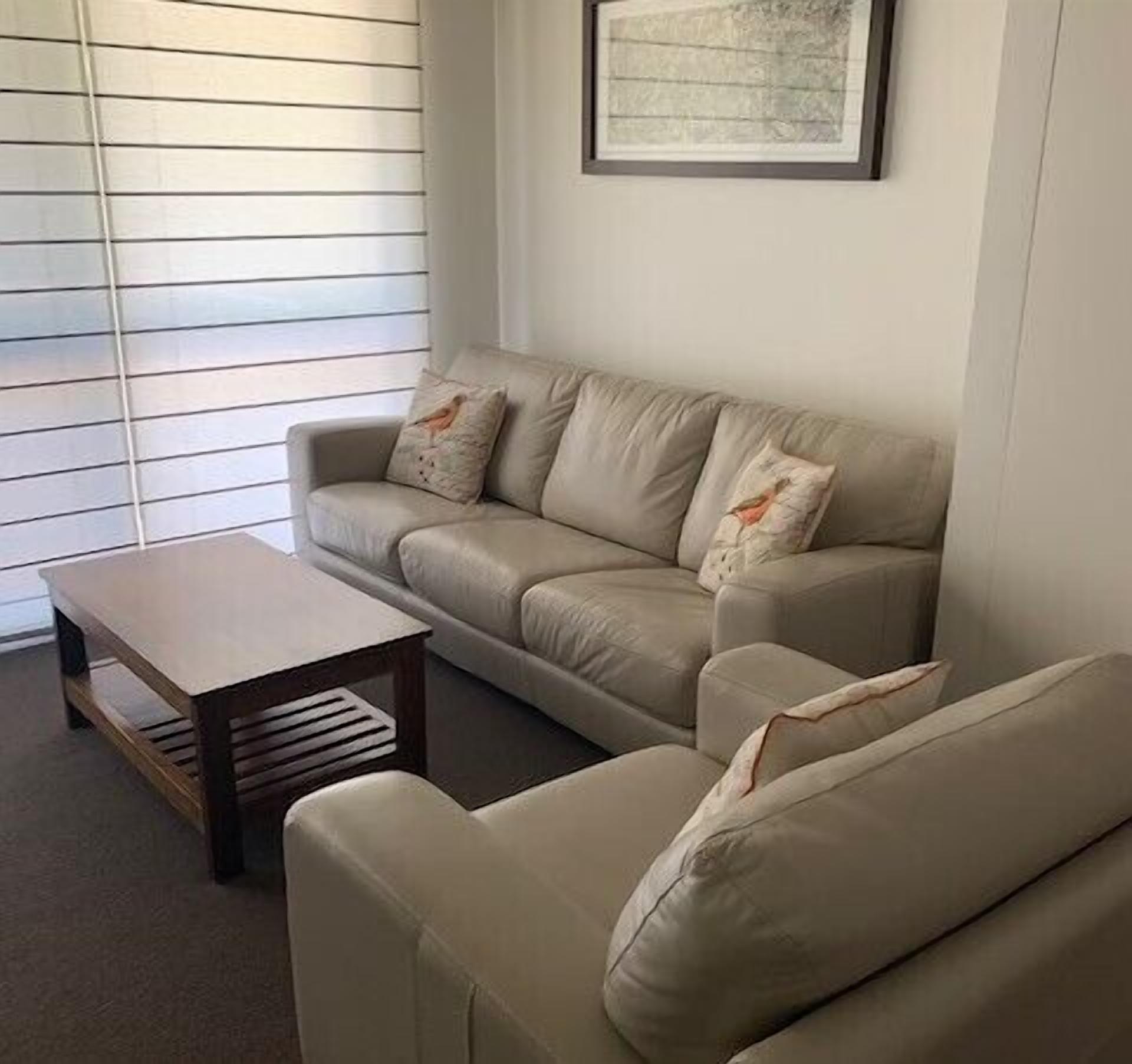 A living room with a beige sofa, two matching armchairs, a wooden coffee table, and a framed picture on the wall.