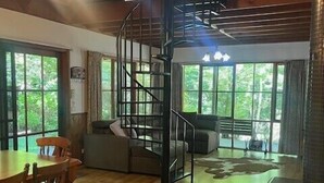 A spacious living area with a wooden floor, a dining table with chairs, a sofa, and a staircase with a metal railing. - Goulburn River Cottage - River Front (Jamieson)