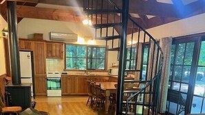 A spacious living area with a wooden floor, a spiral staircase, a dining table with chairs, and a sofa. - Goulburn River Cottage - River Front (Jamieson)