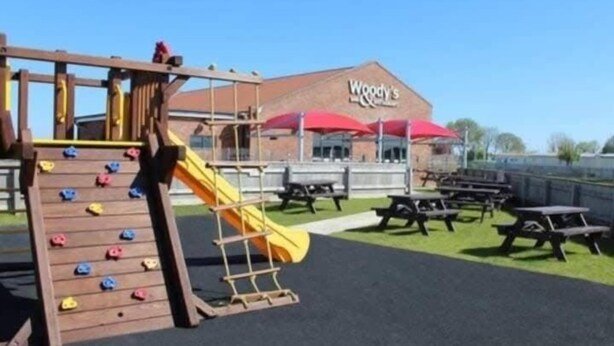 Ein Spielplatz mit Kletterwand und Rutsche, Picknicktischen sowie einem Gebäude mit roter Markise, auf dem 