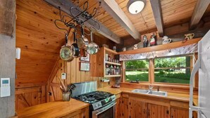Una cocina rústica con paredes de madera, estufa a gas, un lavabo y ventana con vistas a un jardín.