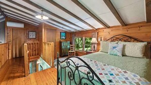 Dormitorio de cabaña de madera con cama, escritorio y ventana con vistas a follaje.