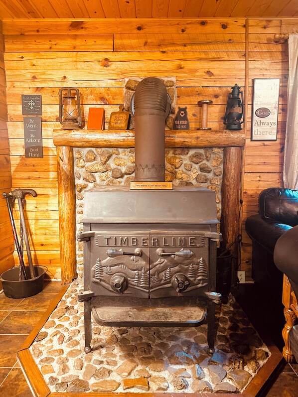 Interior rústico de una cabaña con estufa de leña, chimenea de piedra, paredes de madera y una zona de estar acogedora.
