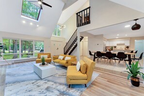 A spacious living area with a modern sofa set, a dining table with chairs, and a staircase leading to an upper level.