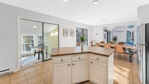 Una cocina moderna con armarios blancos, encimera de madera y comedor con mesa y sillas.