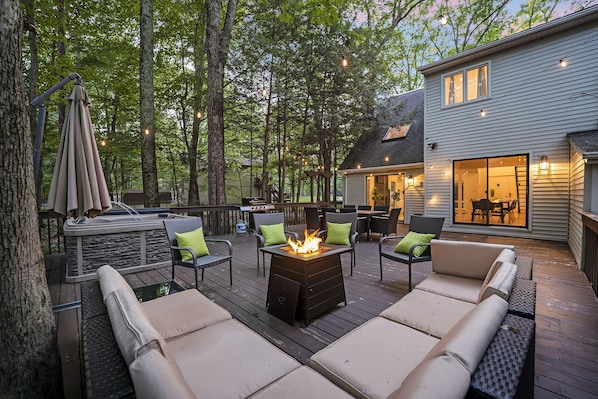 A deck with outdoor seating, a fire pit, and a house in the background.
