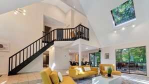 Un salón espacioso con una escalera moderna, asientos cómodos y ventanas amplias con vistas al exterior.