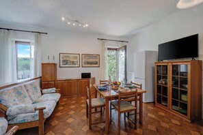 A dining area with a wooden table and chairs, a sofa, a cabinet with glass doors, and a television on the wall.