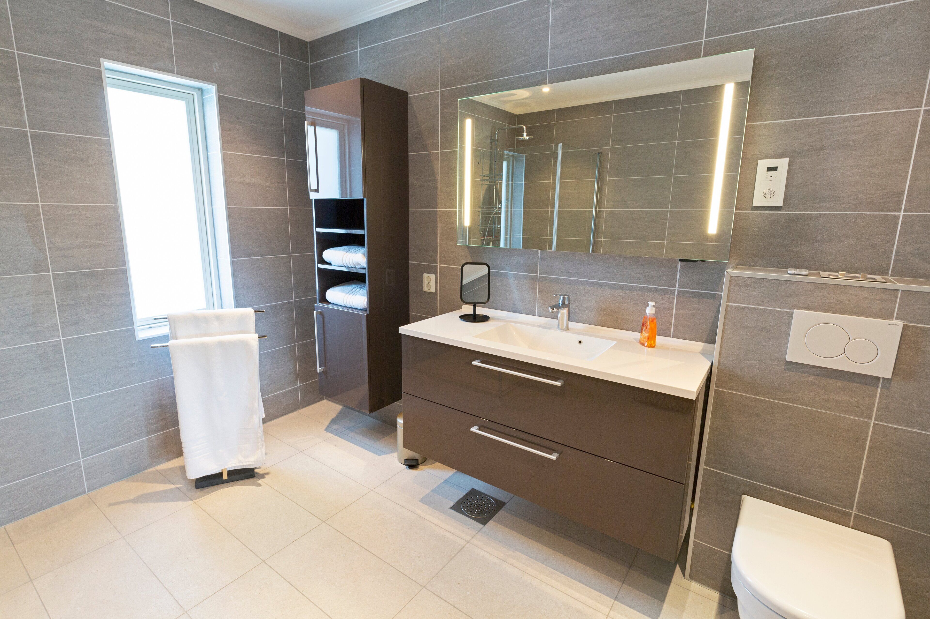 A modern bathroom with a large mirror, a white sink, and a toilet.