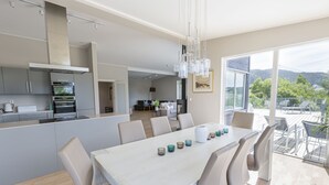 Eine moderne Küche mit eingebauten Geräten, ein Essbereich mit großem Tisch und Stühlen sowie ein Balkon mit Blick auf die umliegende Landschaft.